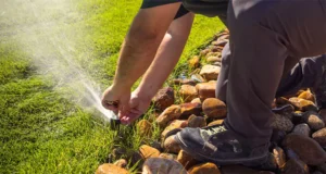 Technician repairing lawn sprinkler system near decorative stone border in Raleigh, NC