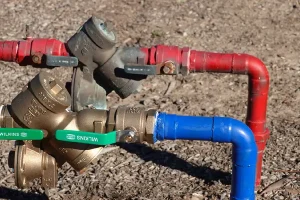 Backflow preventer assembly with red and blue irrigation pipes and shutoff valves installed above ground for residential sprinkler system in Raleigh NC