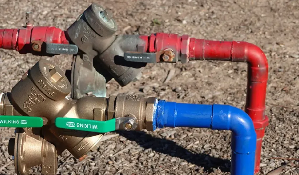 Backflow preventer assembly with red and blue irrigation pipes and shutoff valves installed above ground for residential sprinkler system in Raleigh NC