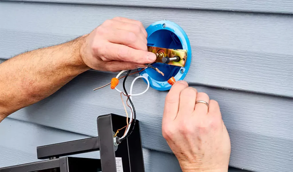 Electrician repairing outdoor landscape lighting wiring on house siding to prevent fixture damage in Raleigh, NC.