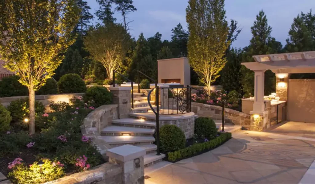 Elegant backyard with custom stone steps, landscape lighting, and a pergola-covered outdoor kitchen at dusk