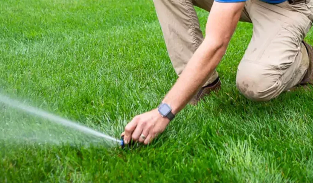 Technician adjusting a lawn sprinkler head to ensure proper water coverage and prevent property damage.
