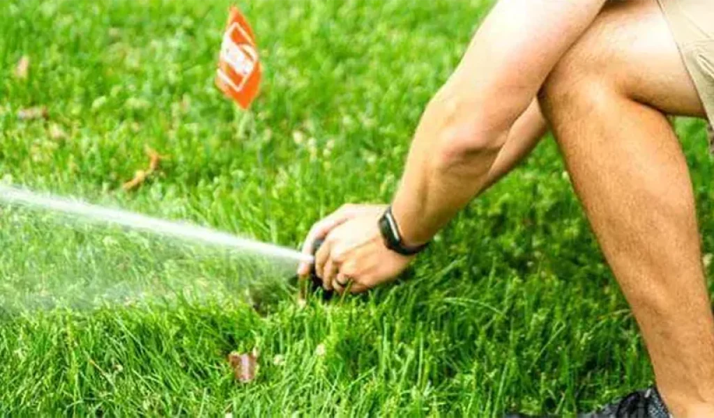 Technician adjusting a sprinkler head spraying water on green grass—demonstrating professional sprinkler system installation and maintenance in Raleigh, NC during summer.